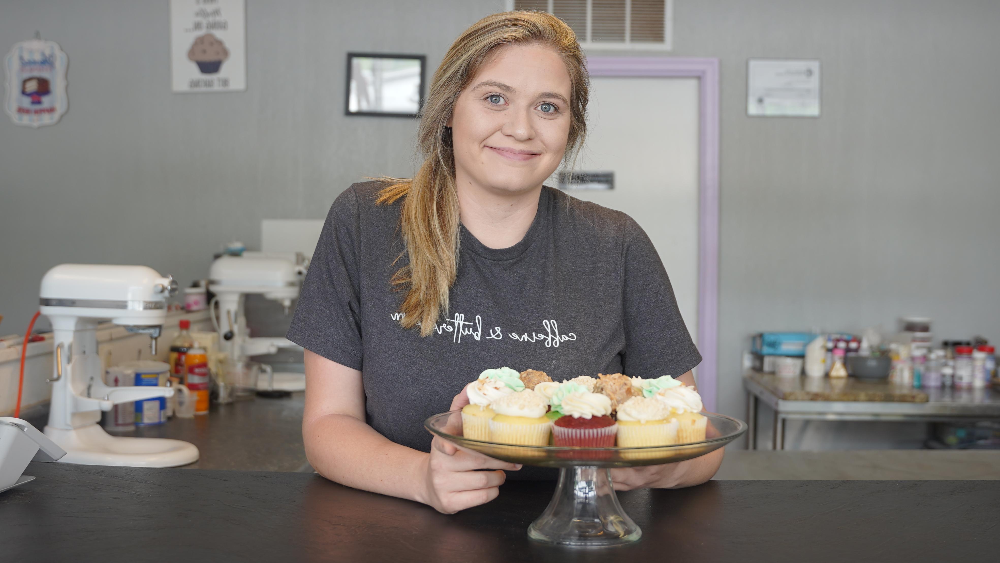 a photograph of Samantha Tichnell, smiling and resting her arms on a surface.  A plate of cupcakes is on the surface in front of her